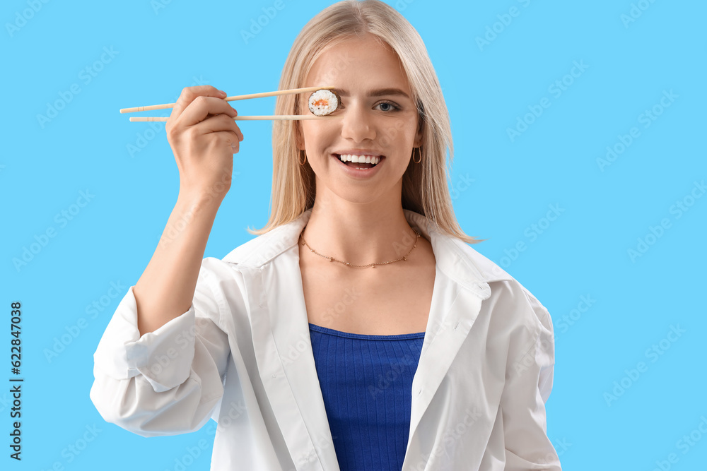 Young woman with tasty sushi roll on blue background