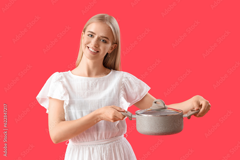 Young woman with cooking pot on red background