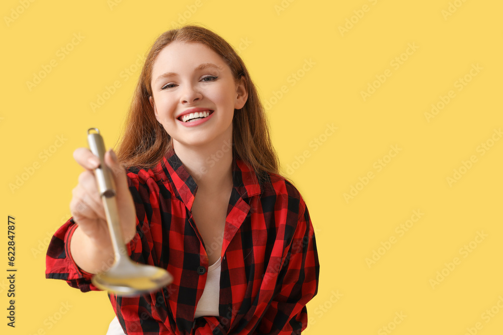 Young woman with ladle on yellow background