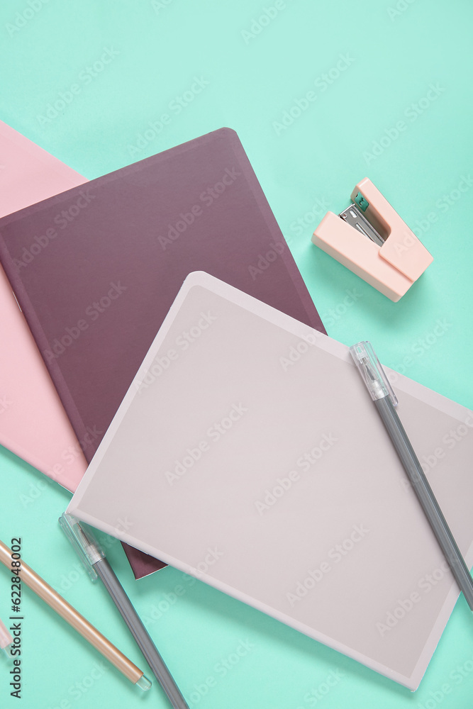 Different colorful notebooks with pens and stapler on turquoise background