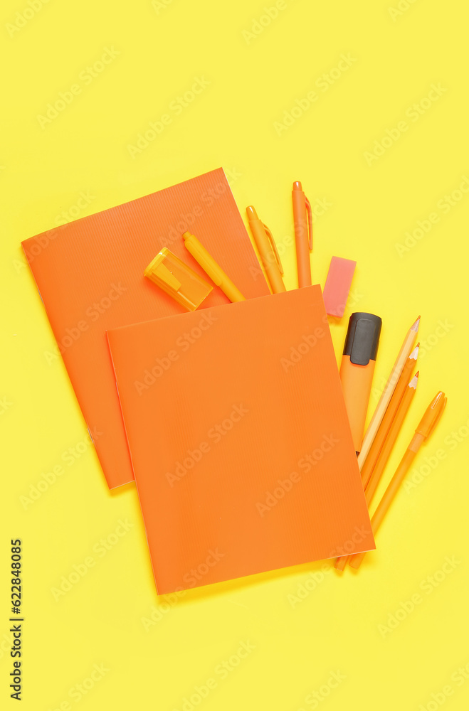 Notebooks with different stationery on yellow background