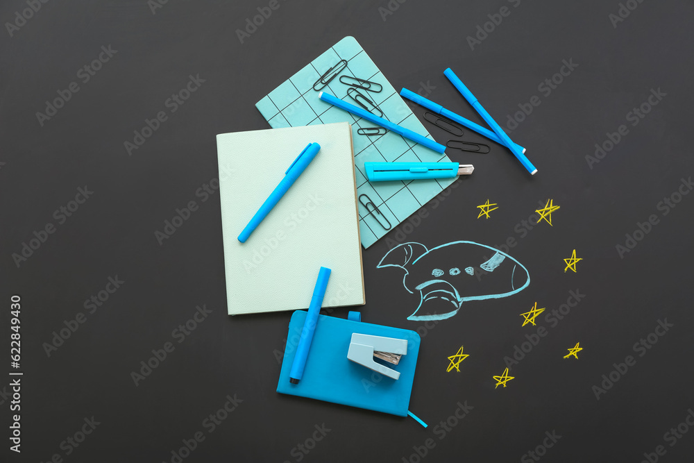 Creative composition with drawn rocket and different stationery on black chalkboard