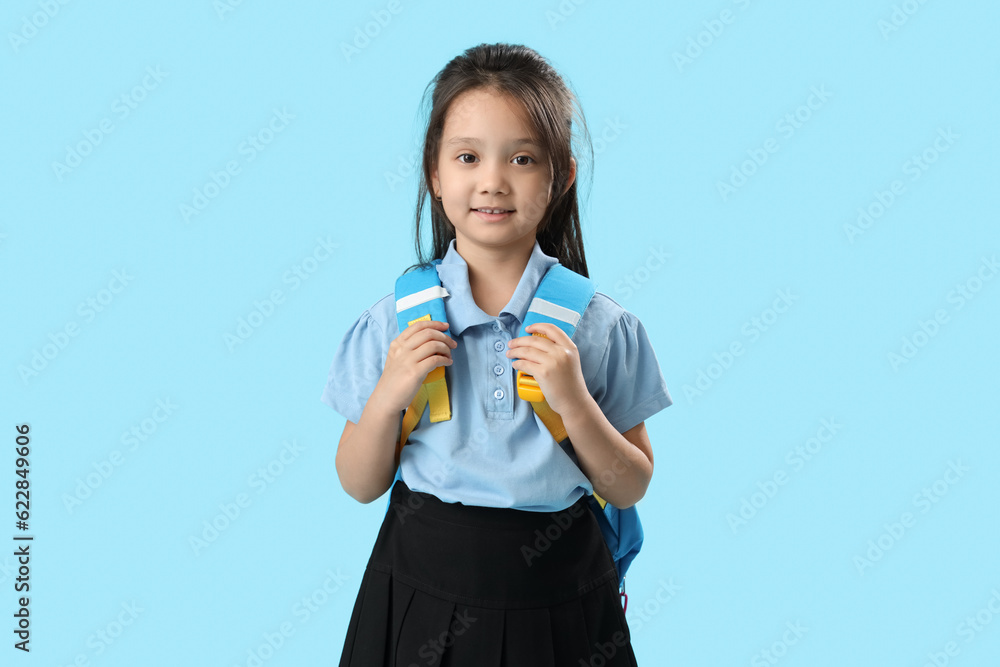 Little schoolgirl with backpack on light blue background