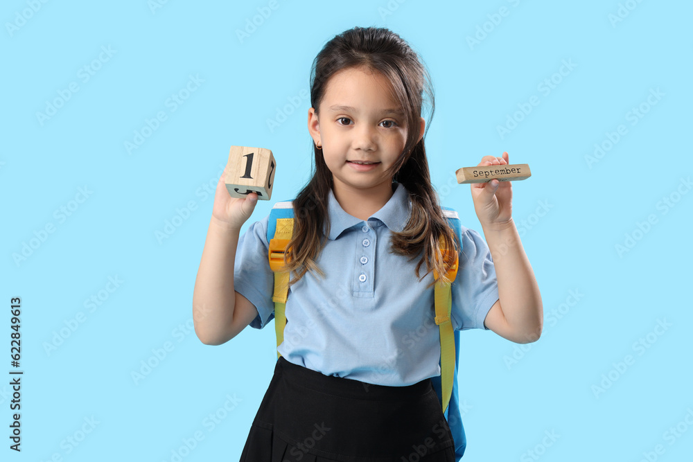 Little schoolgirl with calendar on light blue background