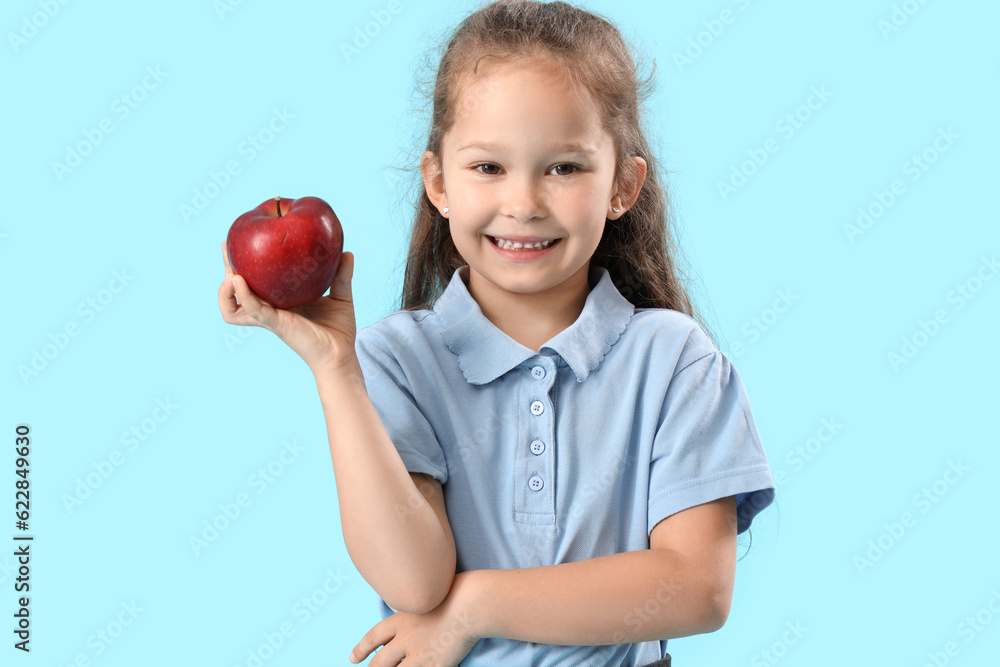 Little schoolgirl with apple on light blue background