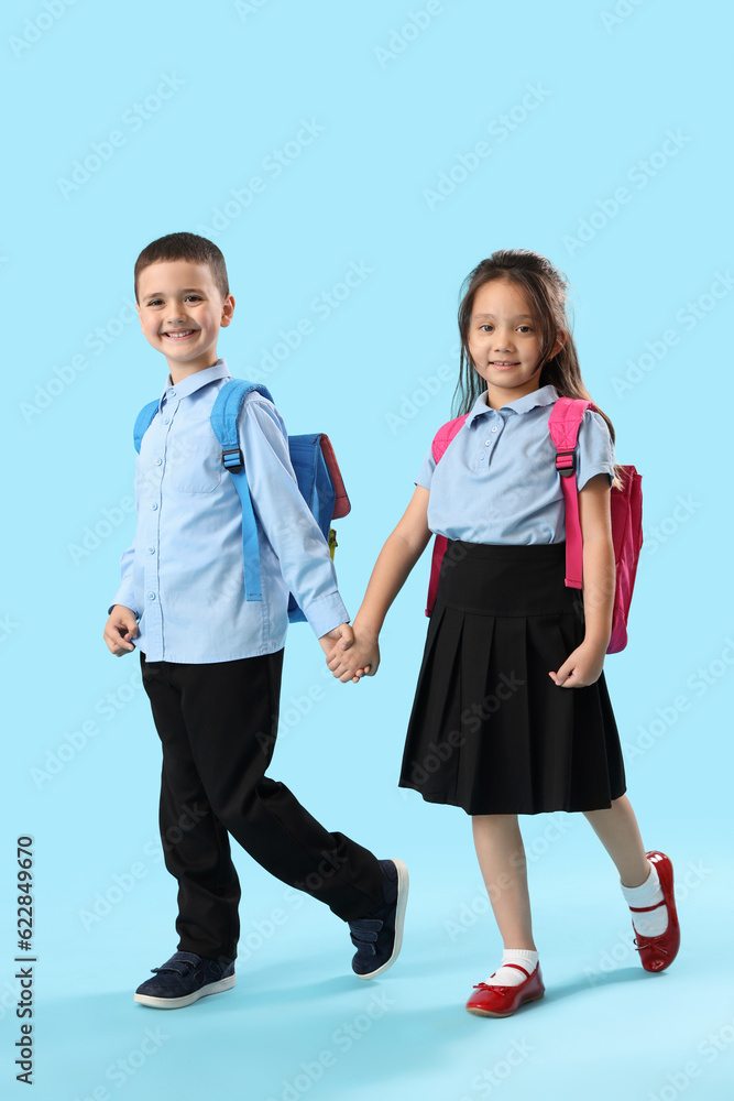 Little schoolchildren holding hands on light blue background