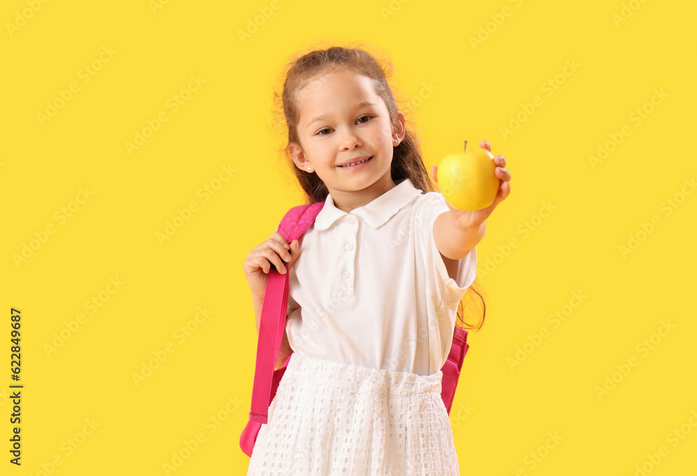 Little schoolgirl with apple on  yellow background