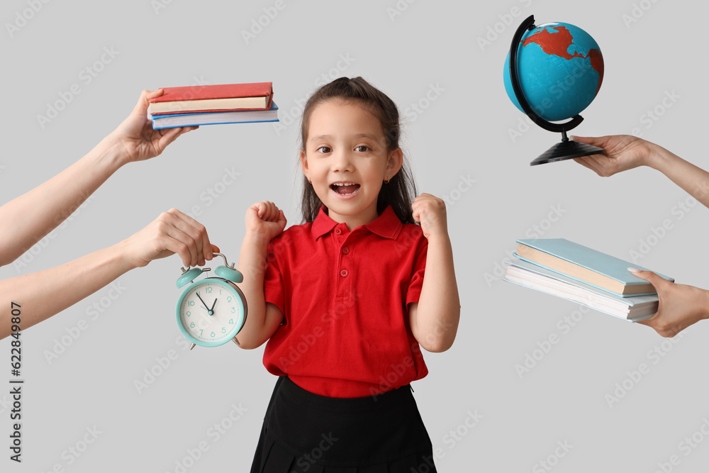 Little schoolgirl and hands holding books, globe and alarm clock on grey background