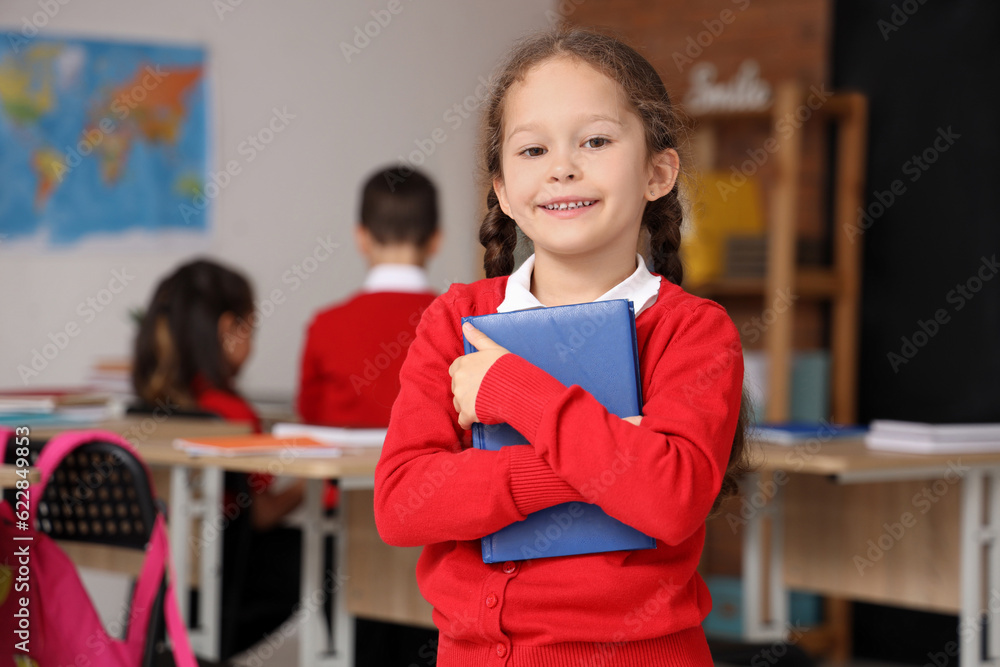 Little schoolgirl with book in classroom