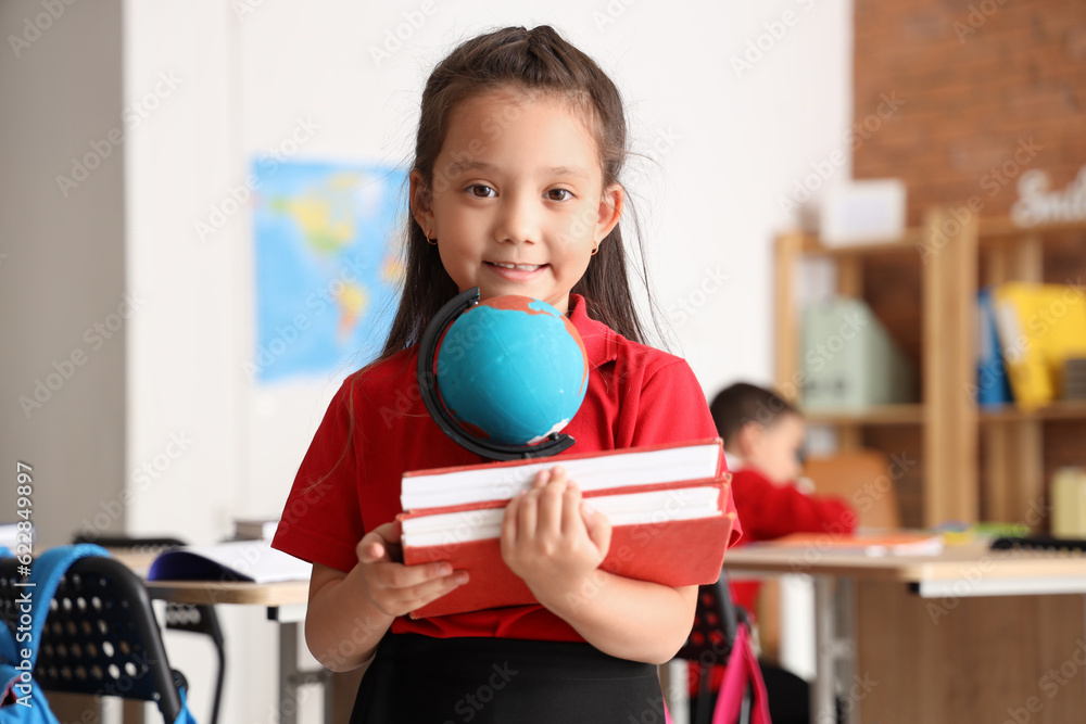 Little schoolgirl with books and globe in classroom