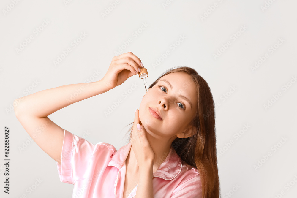 Pretty young woman with cosmetic oil on light background