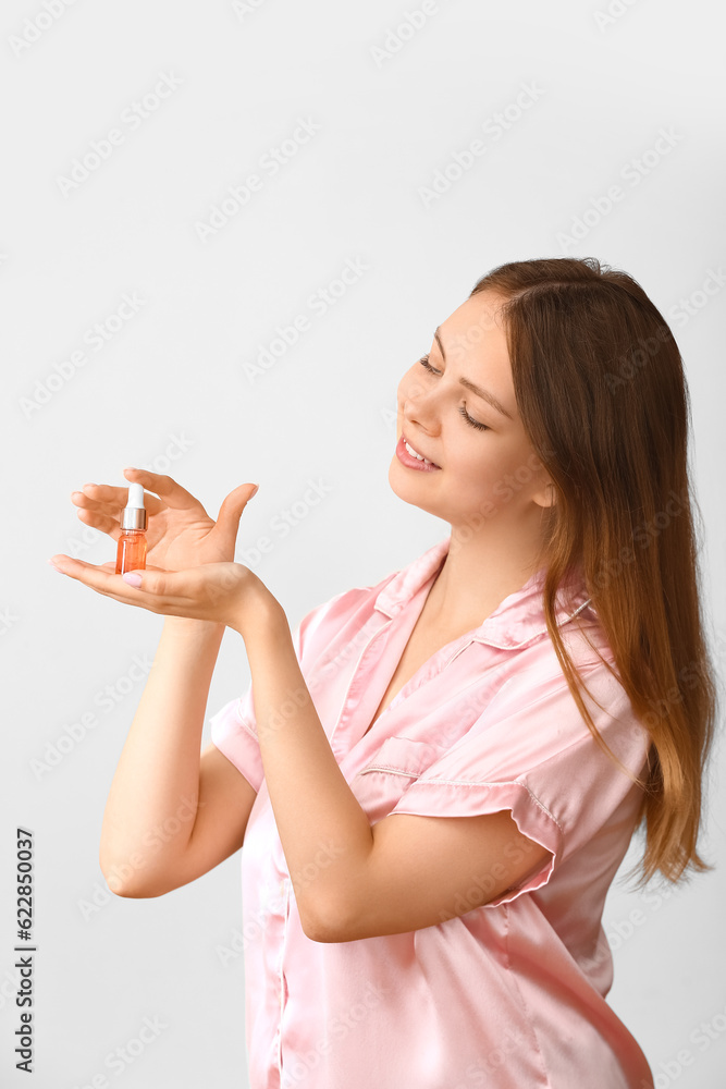 Pretty young woman with cosmetic oil on light background