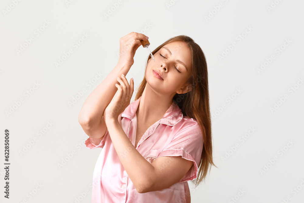 Pretty young woman with cosmetic oil on light background