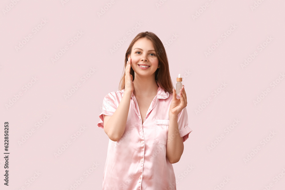 Pretty young woman with cosmetic oil on light pink background