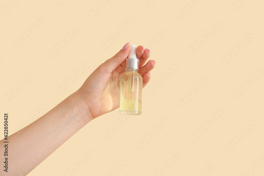 Hand of woman with bottle of cosmetic oil on beige background