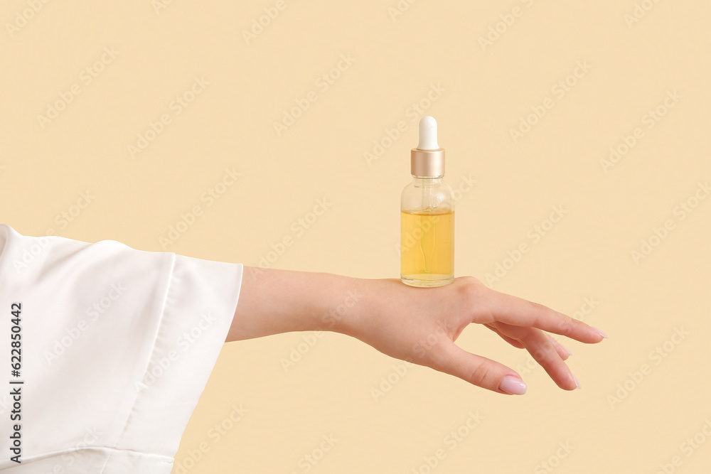 Hand of woman with bottle of cosmetic oil on beige background