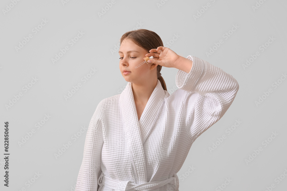 Pretty young woman with cosmetic oil on light background