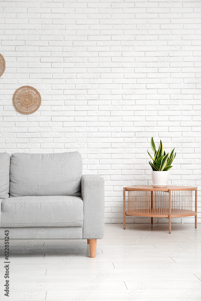 Interior of living room with sofa, table and houseplant near white brick wall