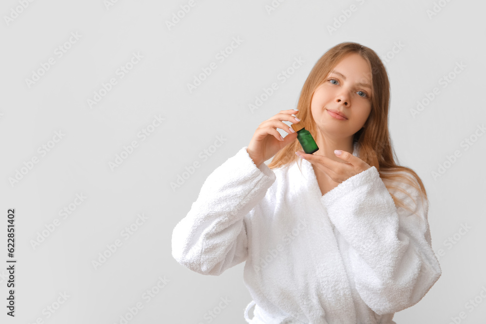 Pretty young woman with cosmetic oil on light background