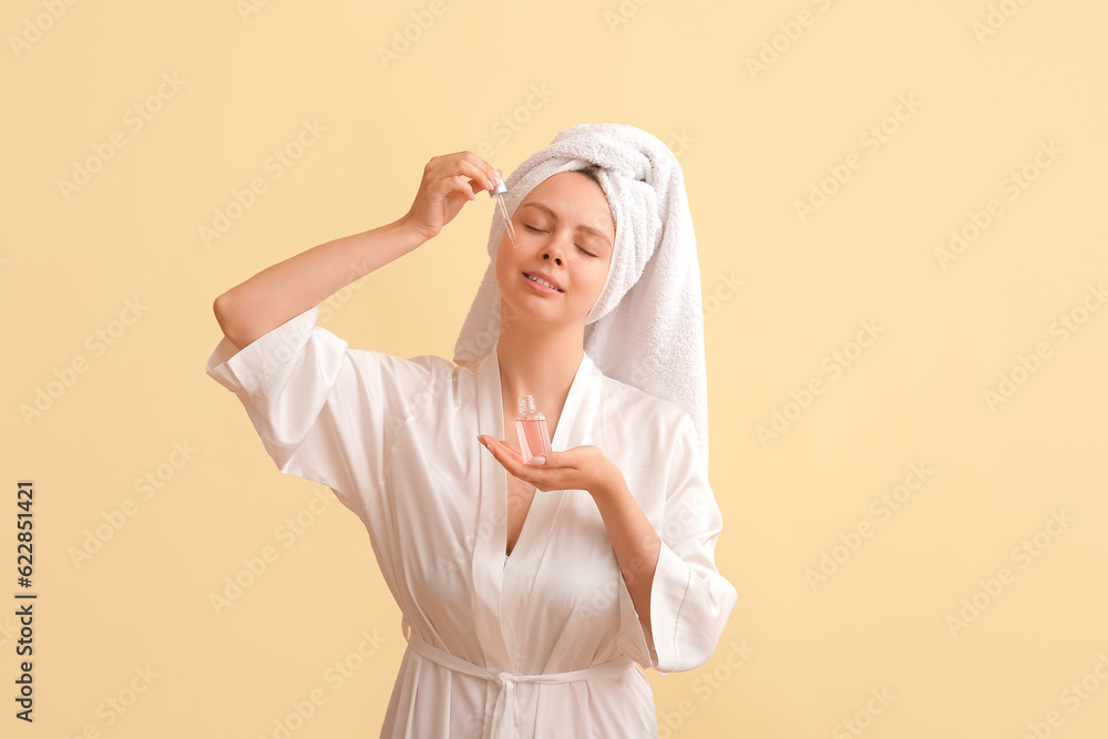 Pretty young woman with cosmetic oil on beige background