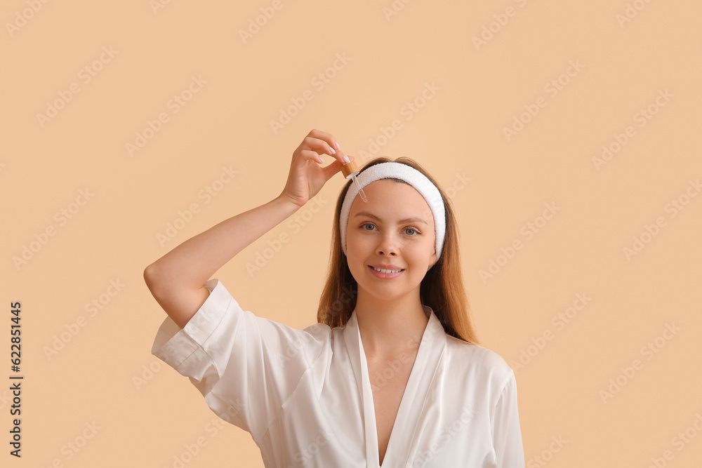 Pretty young woman with cosmetic oil on beige background