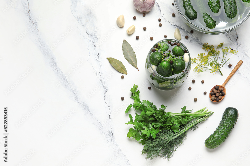 Jar with fresh cucumbers and ingredients for preservation on white marble background