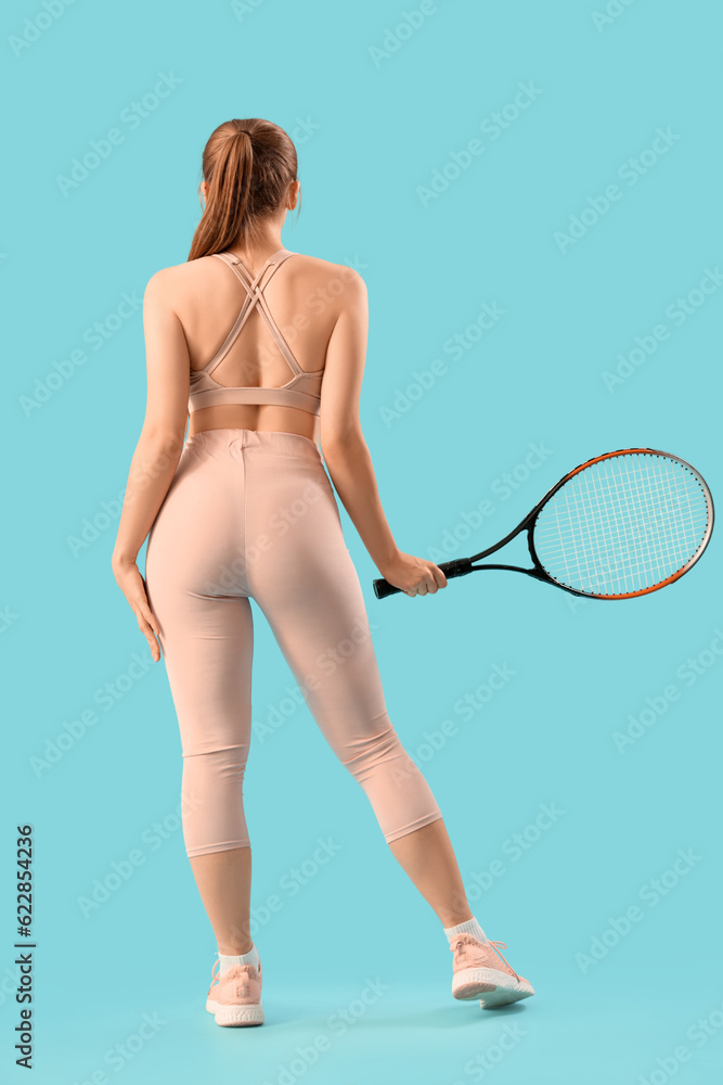 Young woman in sportswear and with tennis racket on light blue background, back view