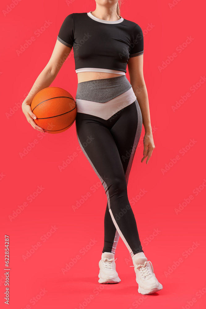 Young woman in sportswear and with ball on red background