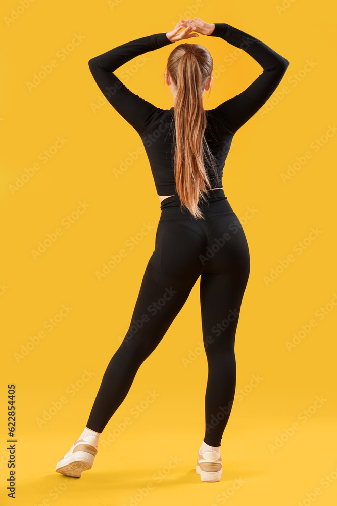 Young woman in sportswear on yellow background, back view