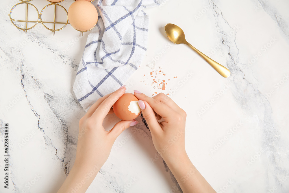 Woman peeling boiled chicken egg on white background