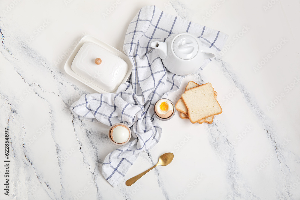 Holders with boiled chicken eggs, bread and teapot on white background