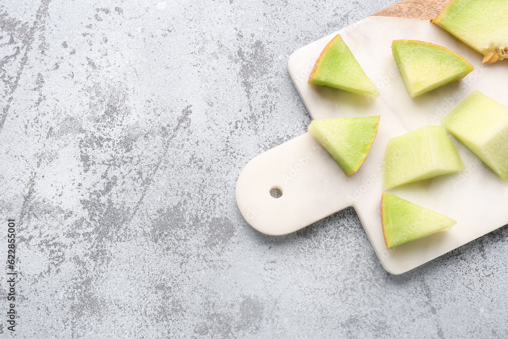 Board with pieces of sweet melon on grey background