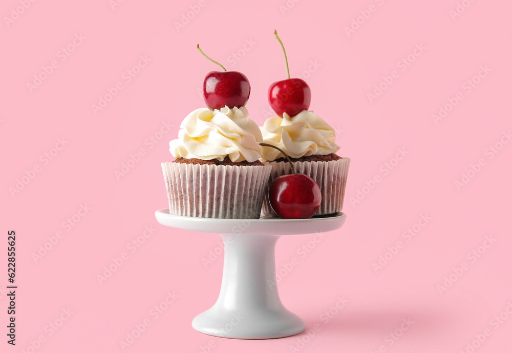 Stand with tasty cherry cupcakes on pink background