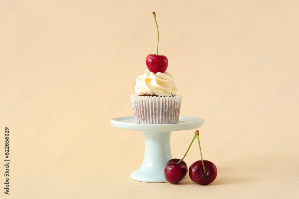 Stand with tasty cherry cupcake on beige background