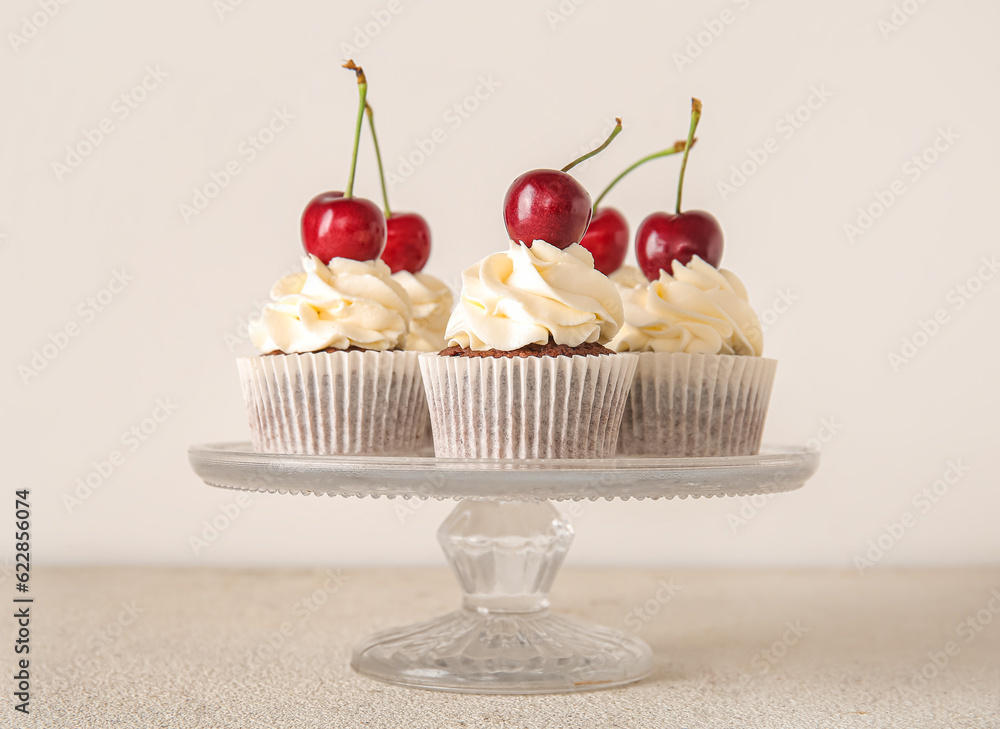 Stand with tasty cherry cupcakes on light background