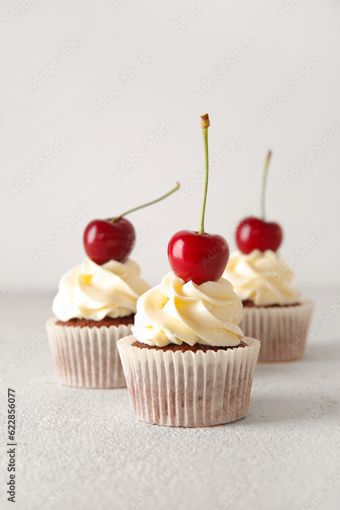 Tasty cherry cupcakes on light background