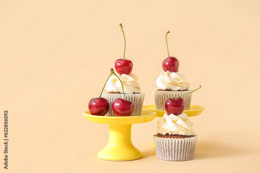 Stands with tasty cherry cupcakes on beige background