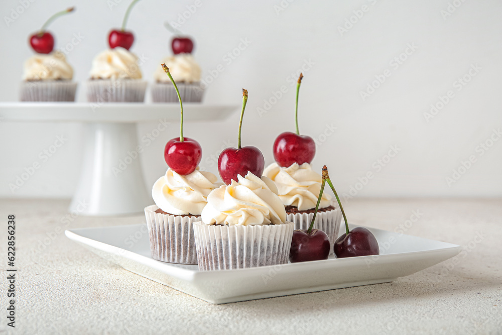 Plate with tasty cherry cupcakes on light background