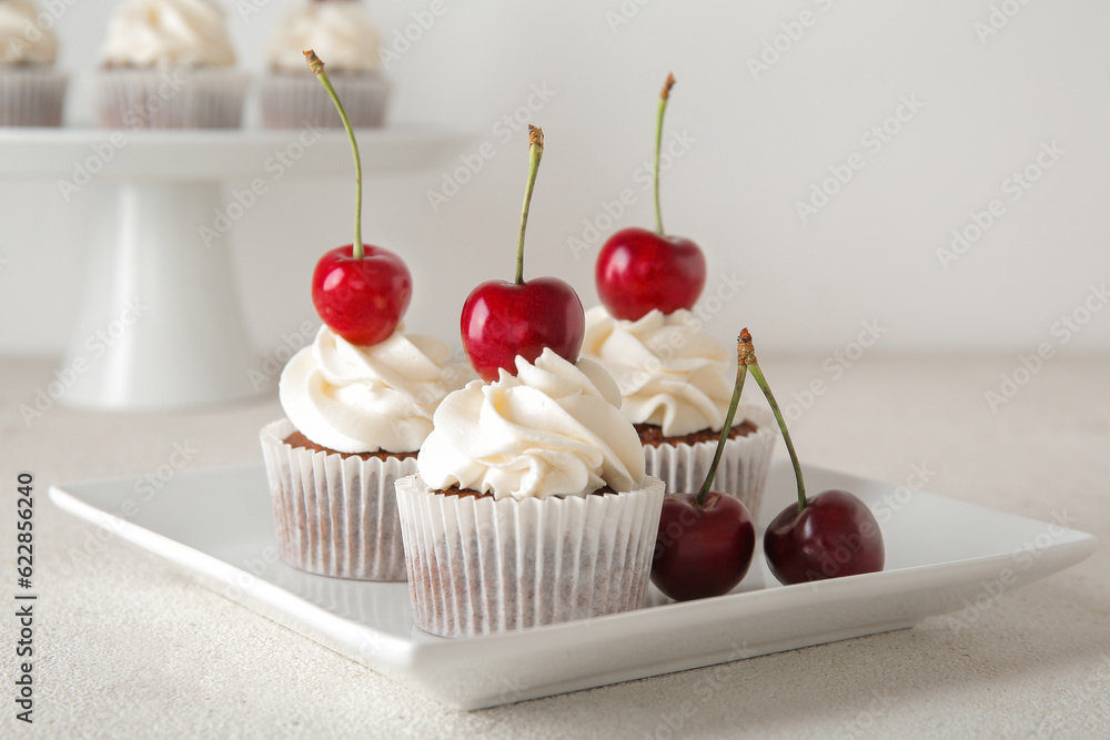 Plate with tasty cherry cupcakes on light background