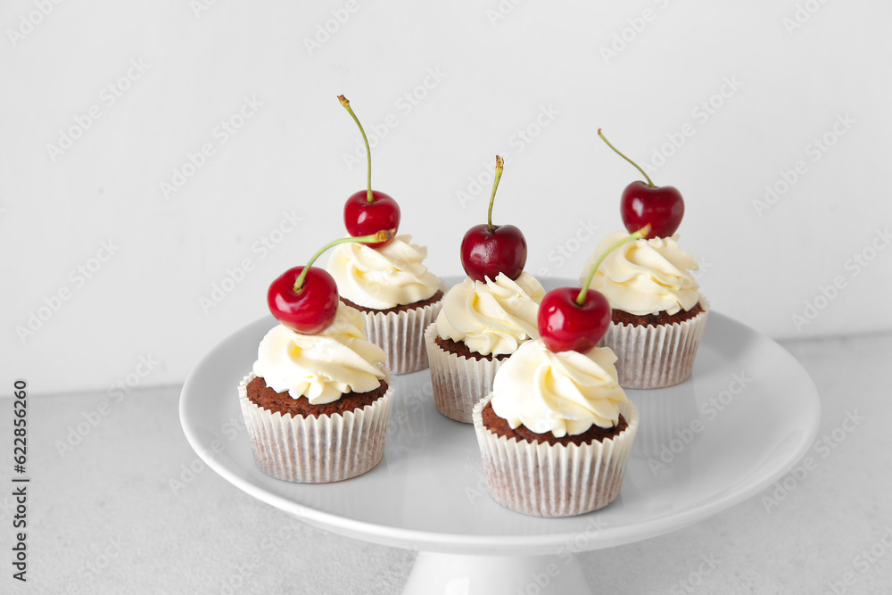 Stand with tasty cherry cupcakes on light background