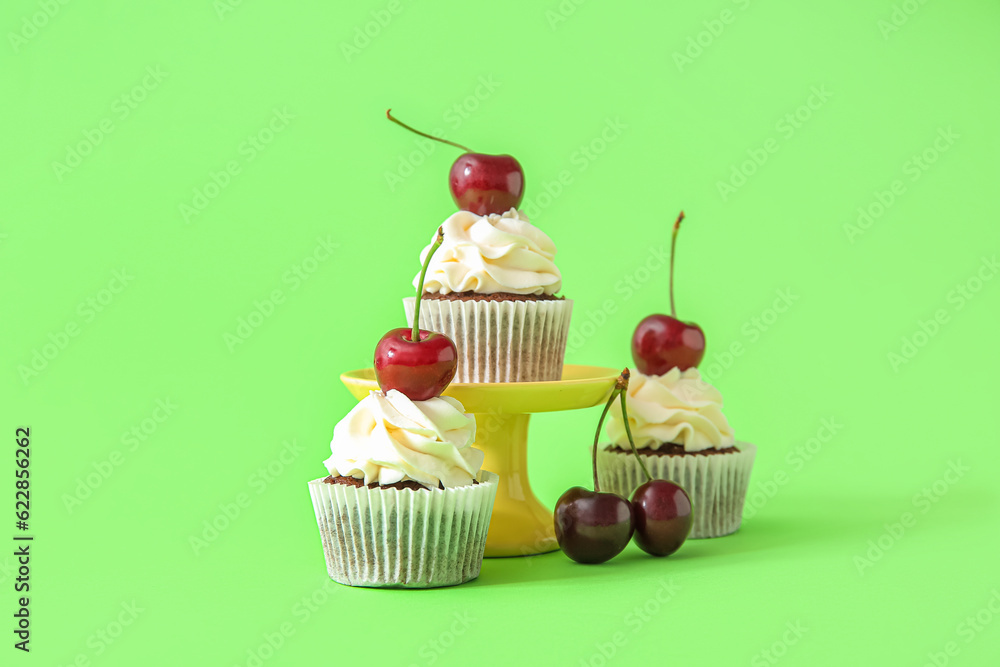 Stand with tasty cherry cupcakes on green background