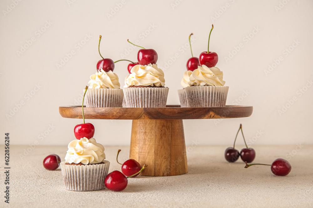 Stand with tasty cherry cupcakes on light background