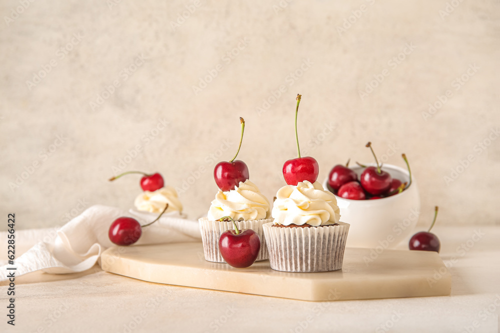 Board with tasty cherry cupcakes on light background