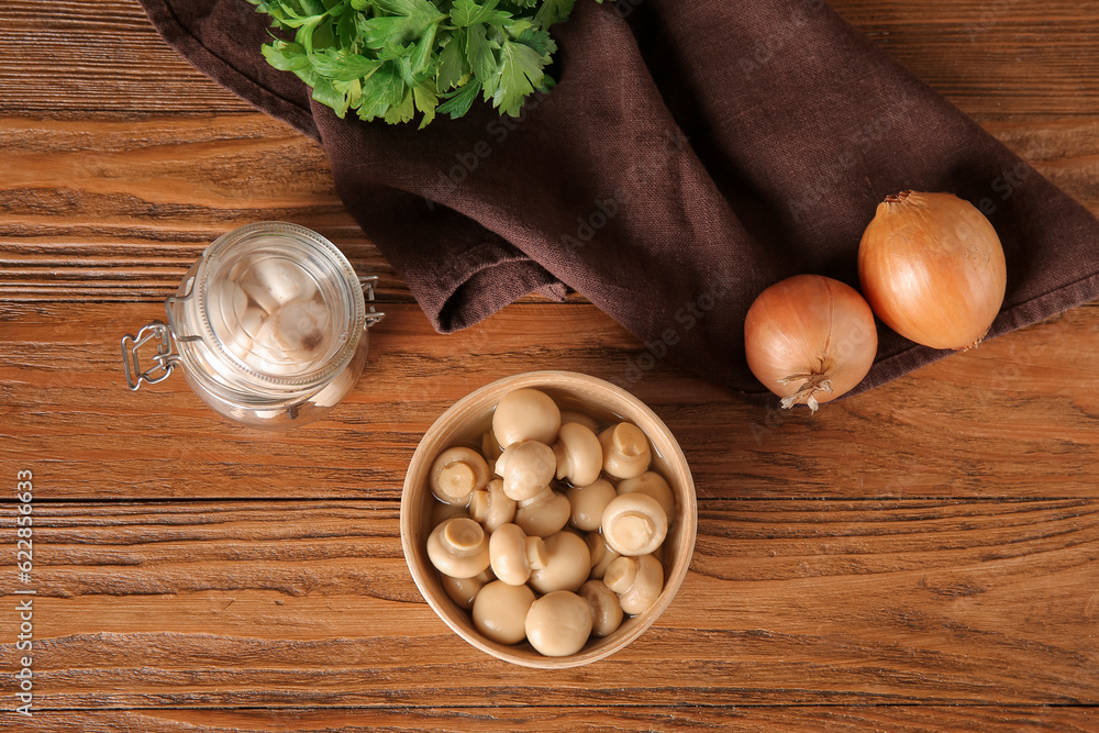 Bowl with canned mushrooms on wooden background