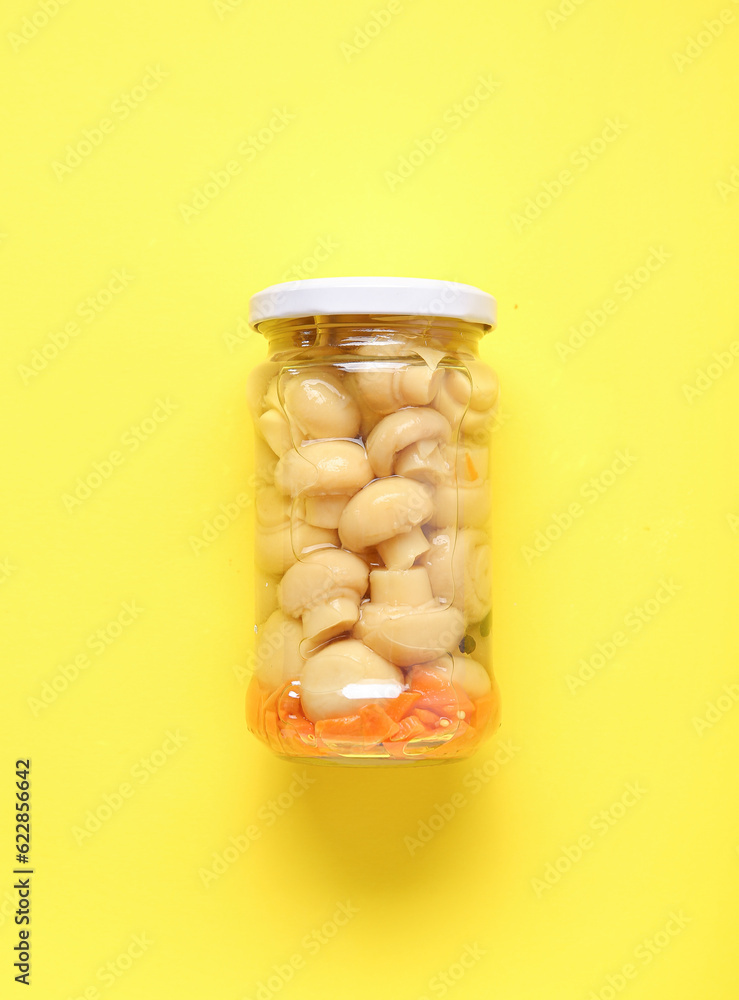 Jar with canned mushrooms on yellow background