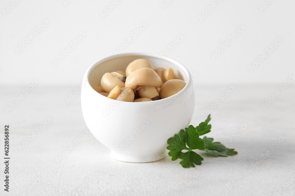 Bowl with canned mushrooms on light background