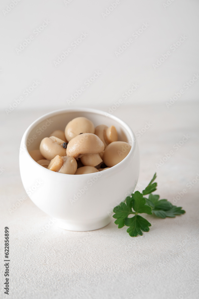 Bowl with canned mushrooms on light background