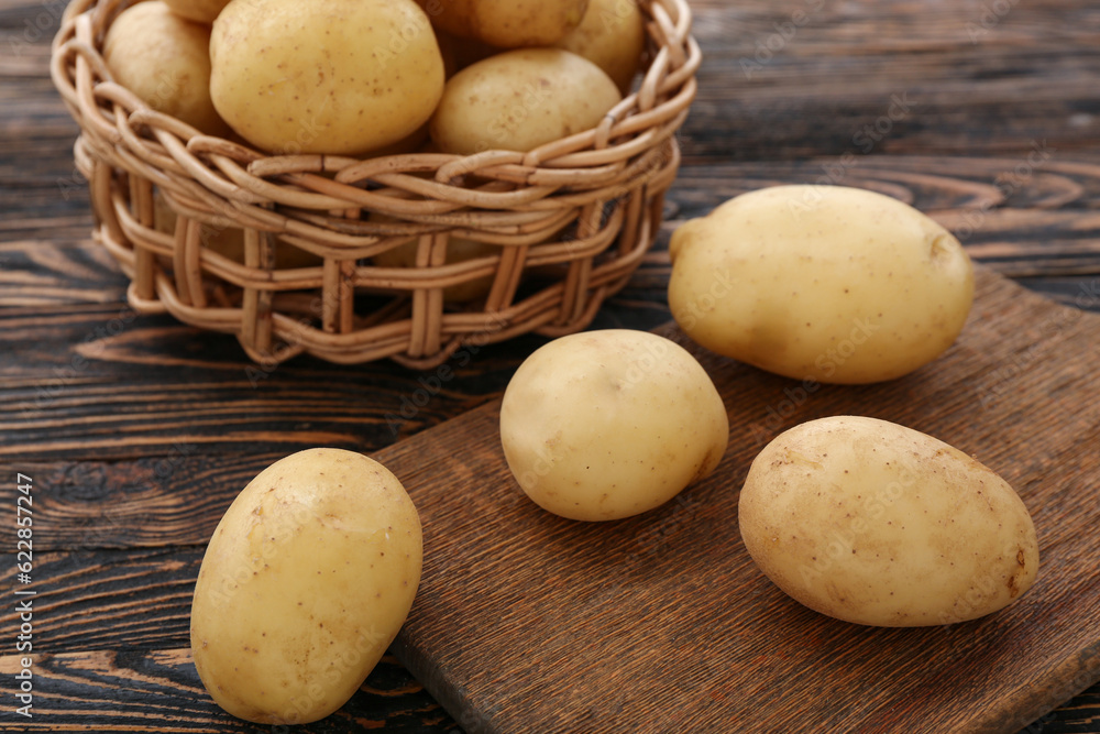 Wicker bowl and board with raw potatoes on wooden background