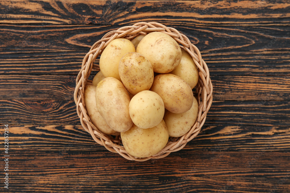 Wicker bowl with raw potatoes on wooden background