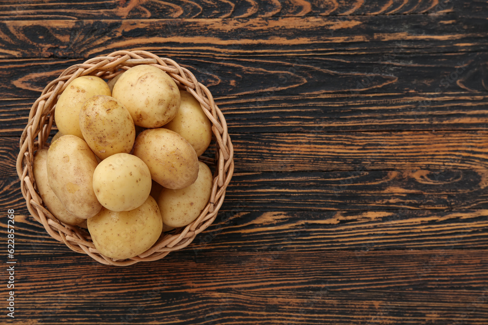 Wicker bowl with raw potatoes on wooden background